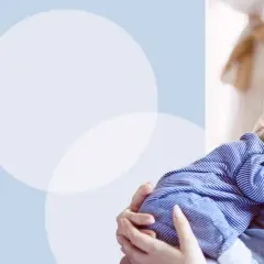 Uśmiechnięta mama tuli śpiącego noworodka w szpitalu. Podpowiadamy, jak ubrać noworodka w szpitalu, by czuł się komfortowo.