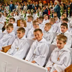 Dzieci w bieli na komunii świętej. Czy rocznica komunii jest obowiązkowa? Rodzice i goście obserwują uroczystość.