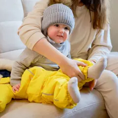 Mama ubiera dziecko w żółty kombinezon i czapkę. Wskazówki, jak ubrać dziecko odpowiednio do temperatury, pomogą Ci przygotować malucha na spacer.