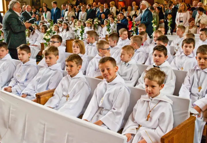 Dzieci w bieli na komunii świętej. Czy rocznica komunii jest obowiązkowa? Rodzice i goście obserwują uroczystość.