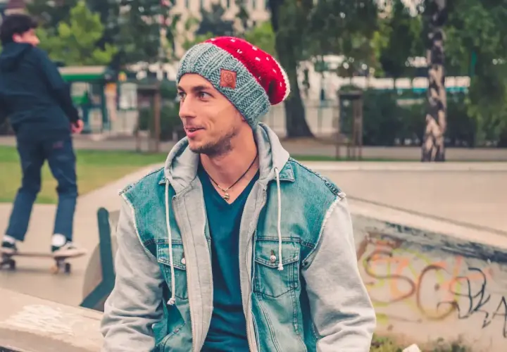 Chłopak w fajnej czapce dla chłopców i jeansowej kurtce siedzi na skateparku.