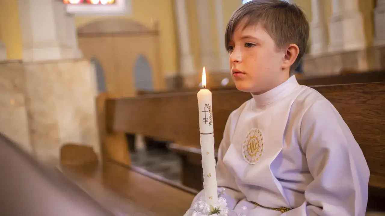 Chłopiec w albie trzyma płonącą świecę. Czy rocznica komunii jest obowiązkowa? Zastanawia się, patrząc w dal.