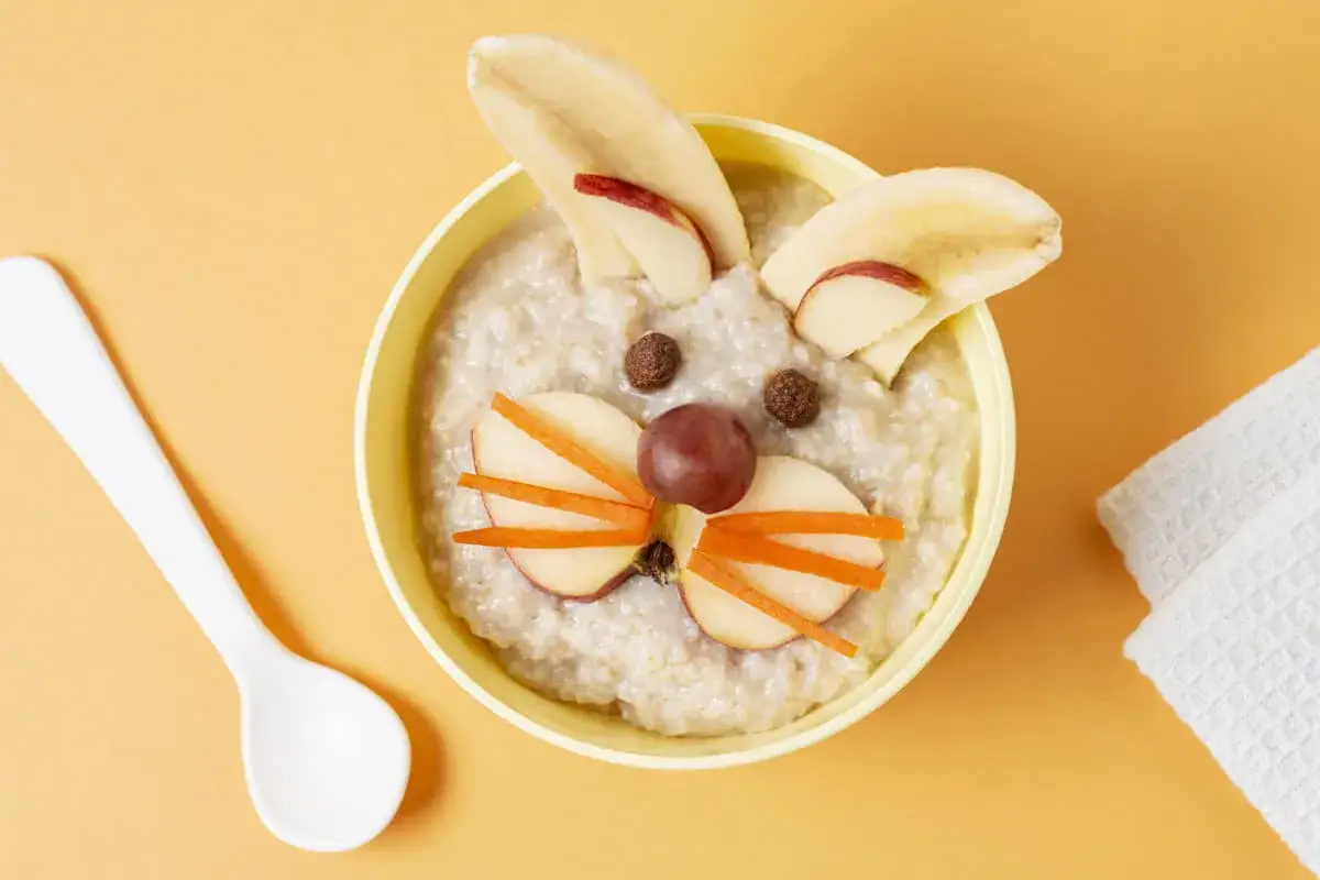 Pyszna owsianka w kształcie królika, idealna jako co na kolację dla 3 latka. Uszy z banana, oczy z czekoladowych kulek, nosek z winogrona i wąsy z marchewki.
